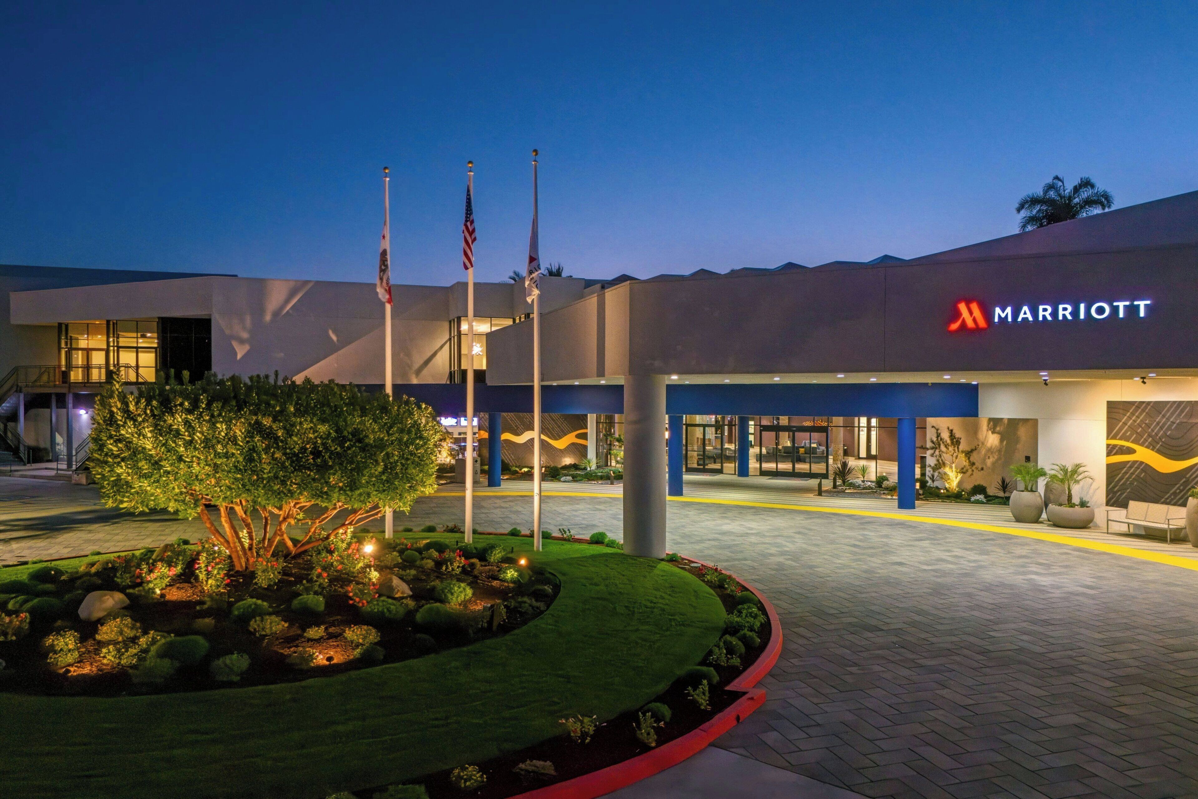 A Marriott hotel entrance with flags, a landscaped garden, and a modern building facade.