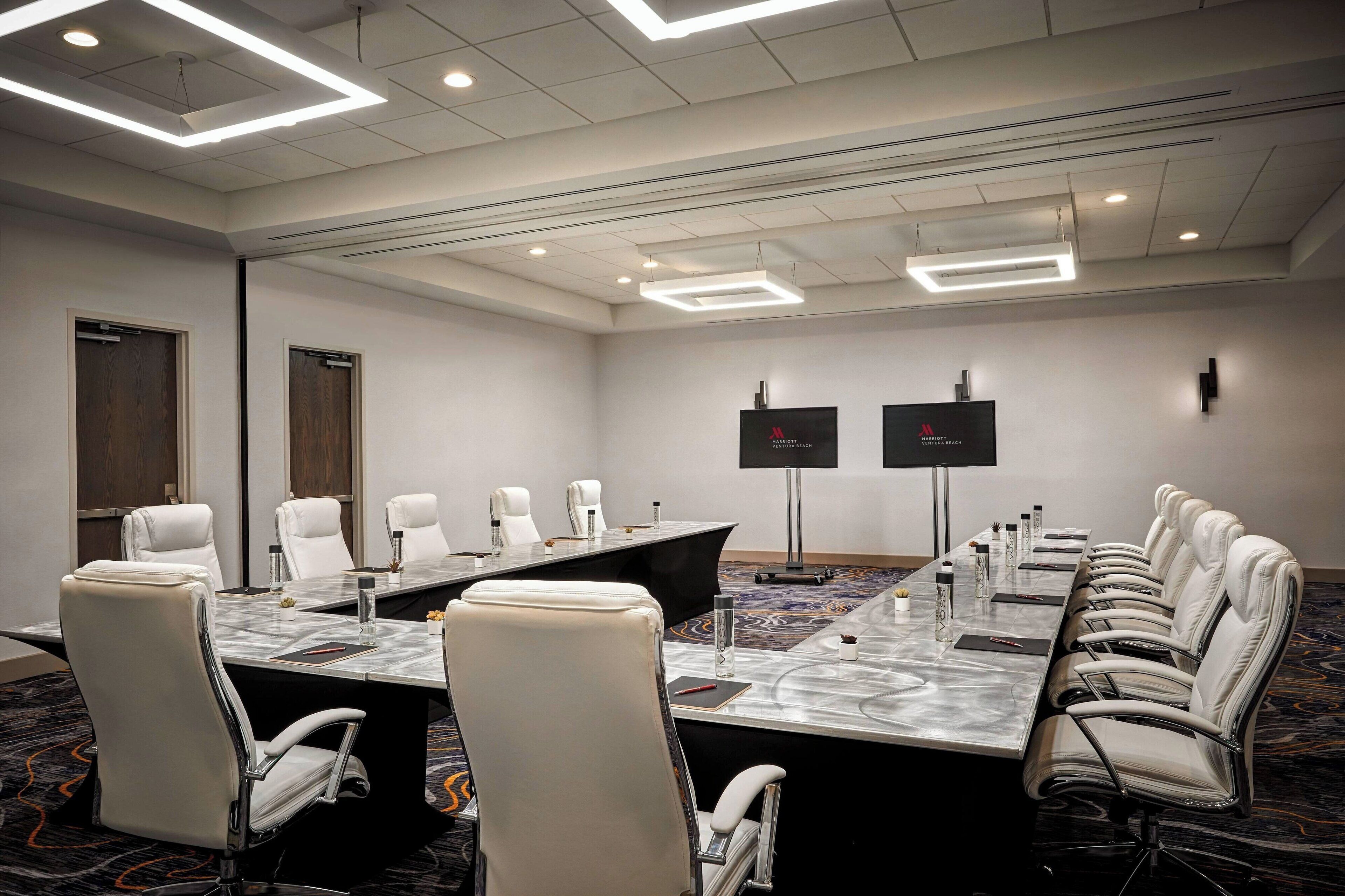 A conference room with a long table, multiple chairs, and a carpeted floor.