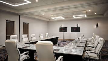 A conference room with a long table, multiple chairs, and a carpeted floor.