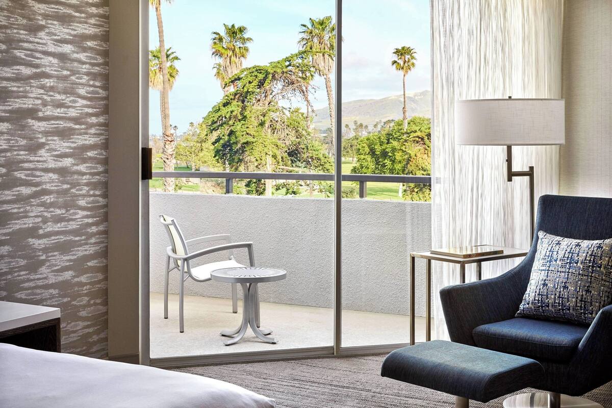 Une chambre d’hôtel avec un balcon, une chaise, une table et une lampe.