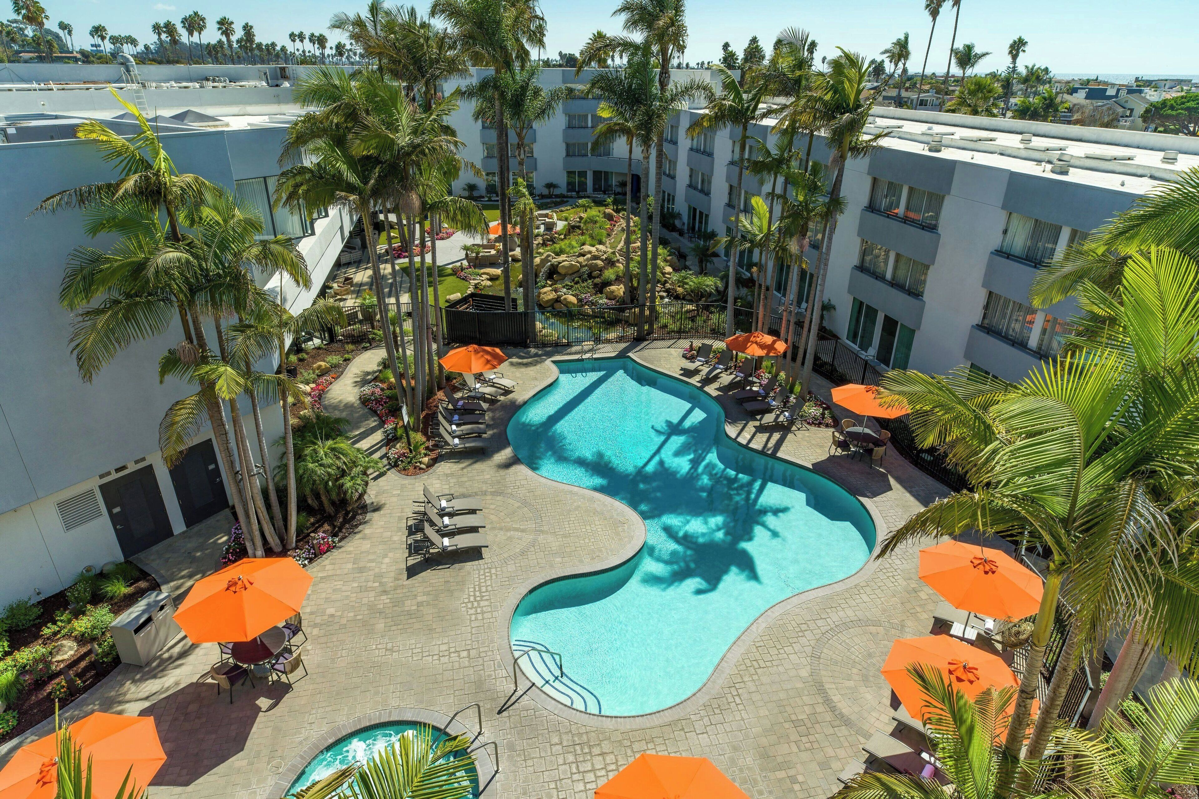 A swimming pool surrounded by palm trees and lounge chairs with orange umbrellas.