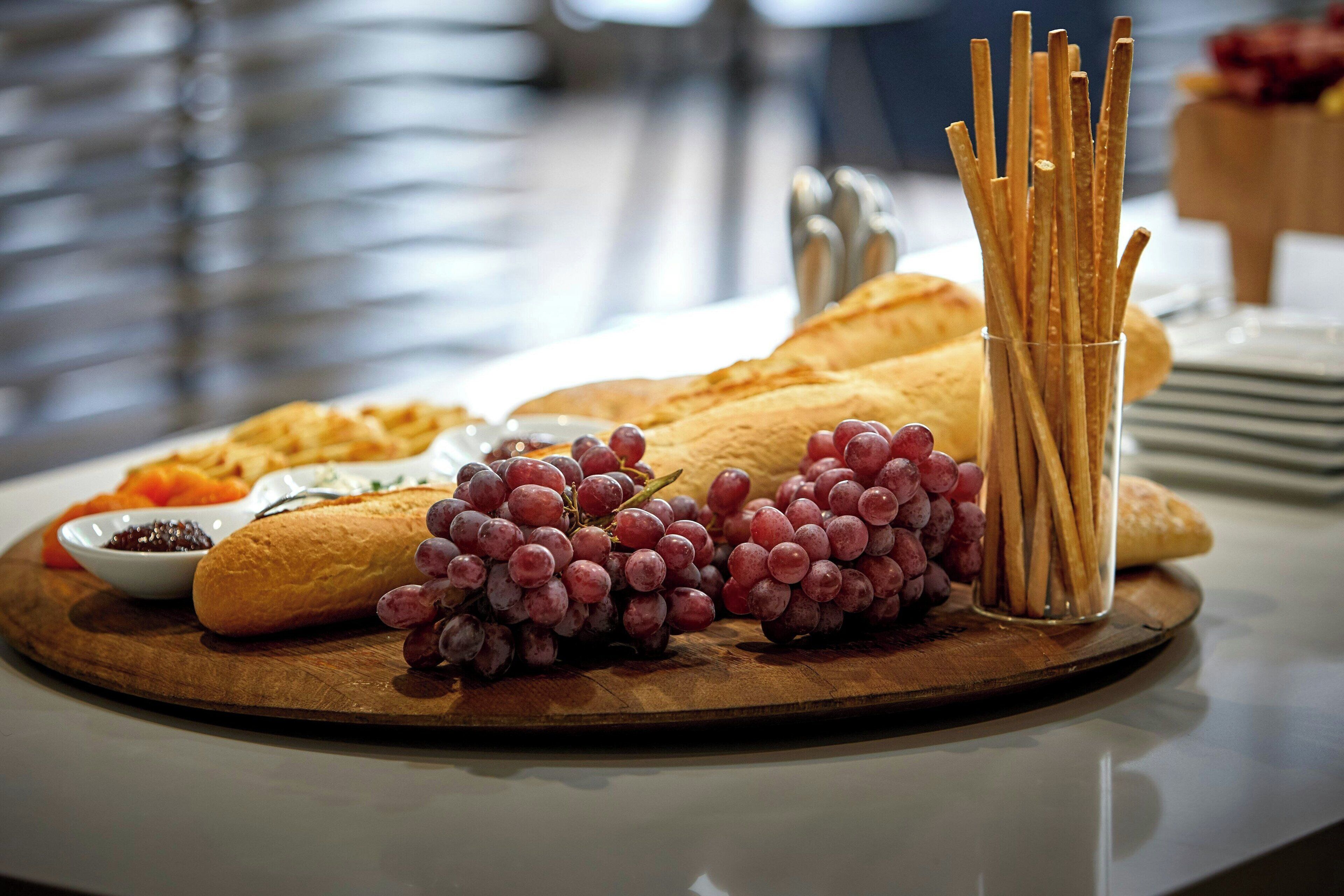 A wooden board with bread, grapes, and crackers on a table.