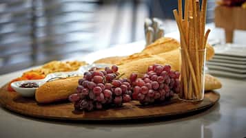 A wooden board with bread, grapes, and crackers on a table.