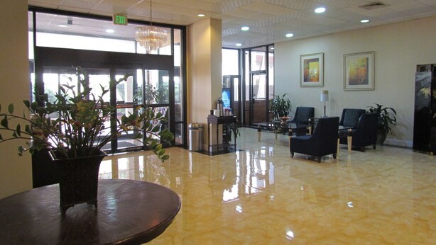 Un vestíbulo amplio con piso pulido, una mesa de recepción, varias sillas y una planta en maceta.