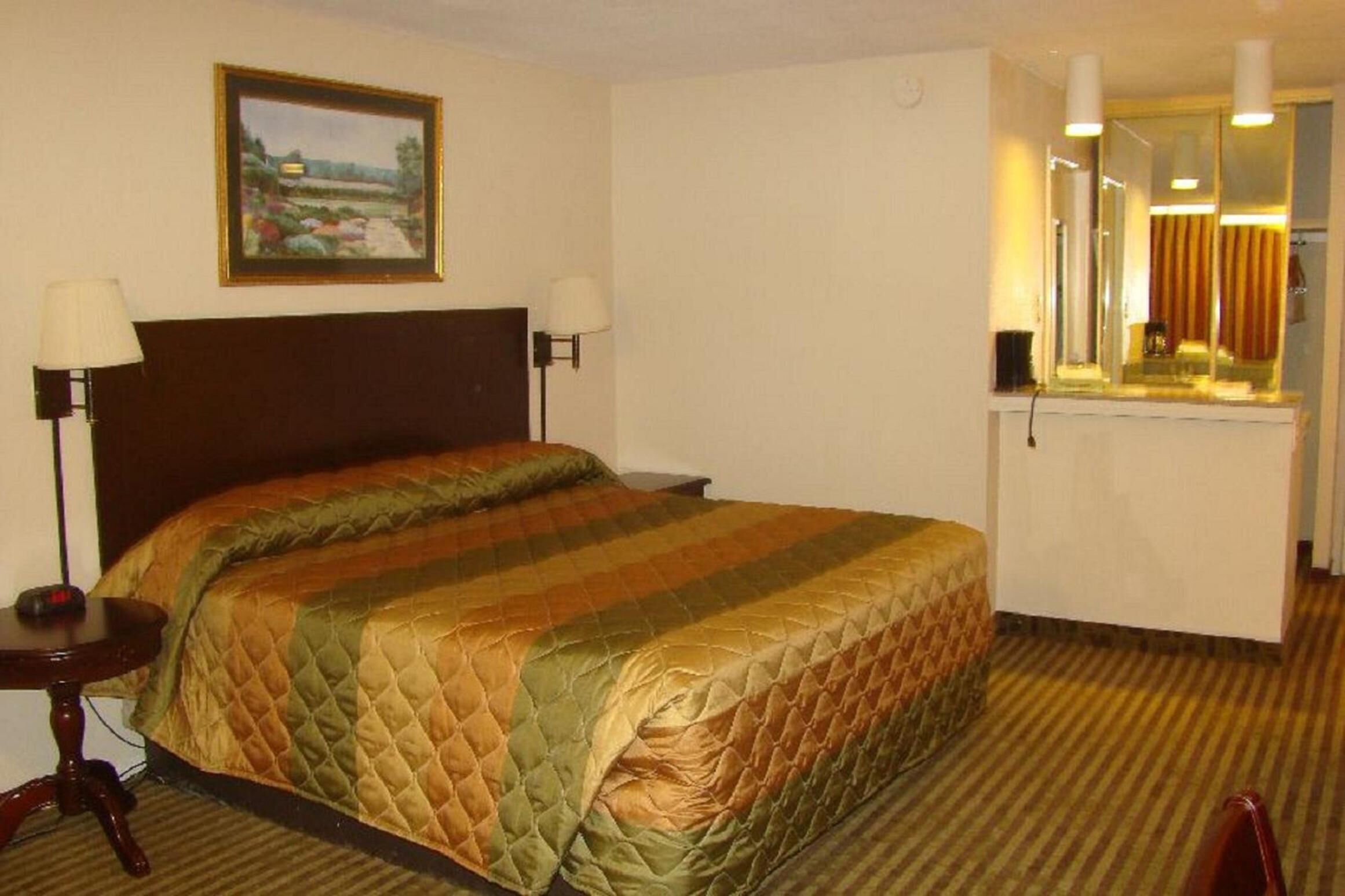 Habitación de hotel con cama, dos lámparas de noche, un cuadro en la pared, un espejo sobre la cama y una ventana con cortinas.