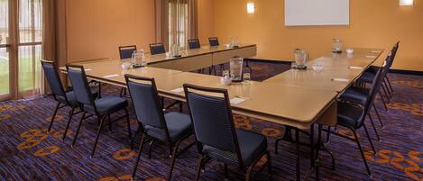 A conference room with a long table, chairs, a projector screen, and a carpeted floor.