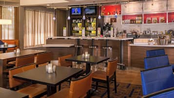 Un bar d’hôtel doté de plusieurs espaces pour s’asseoir, d’un comptoir et d’un écran de télévision diffusant un programme d’information.