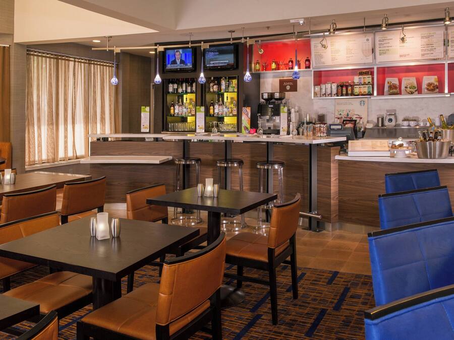 Un bar d’hôtel doté de plusieurs espaces pour s’asseoir, d’un comptoir et d’un écran de télévision diffusant un programme d’information.