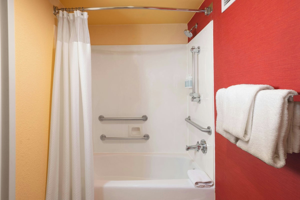 Un baño con ducha, barras de apoyo, un perchero y pared roja.