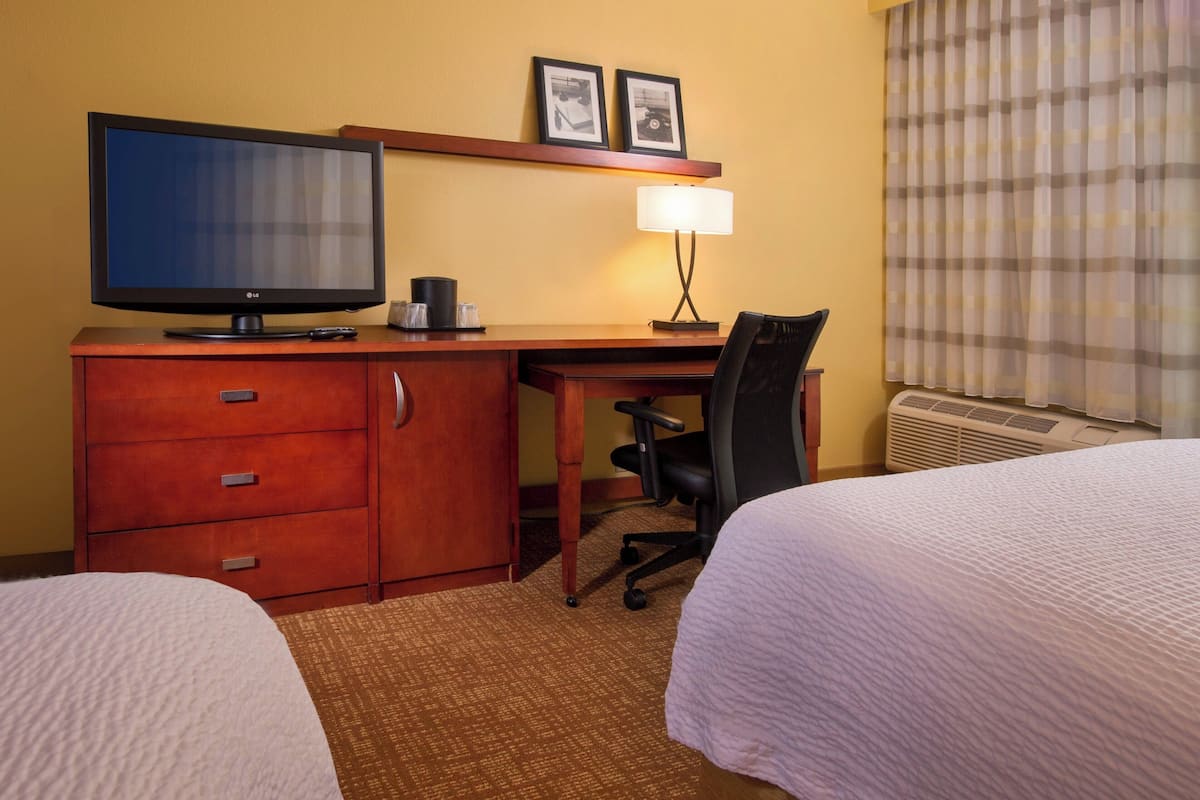 Habitación de hotel con dos camas, un escritorio con televisor, una lámpara y una silla.