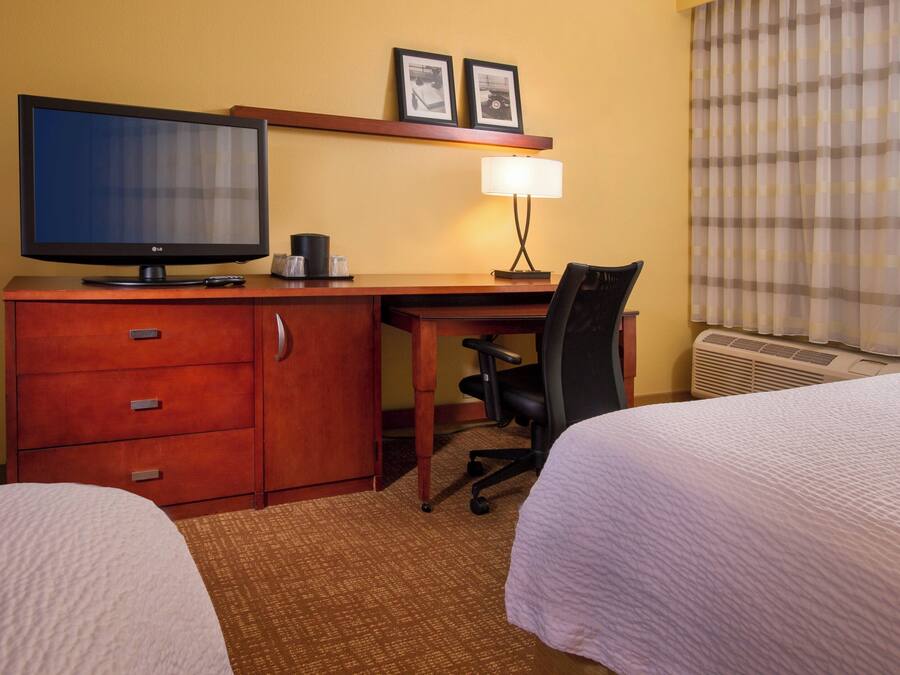 A hotel room with two beds, a desk with a television, a lamp, and a chair.