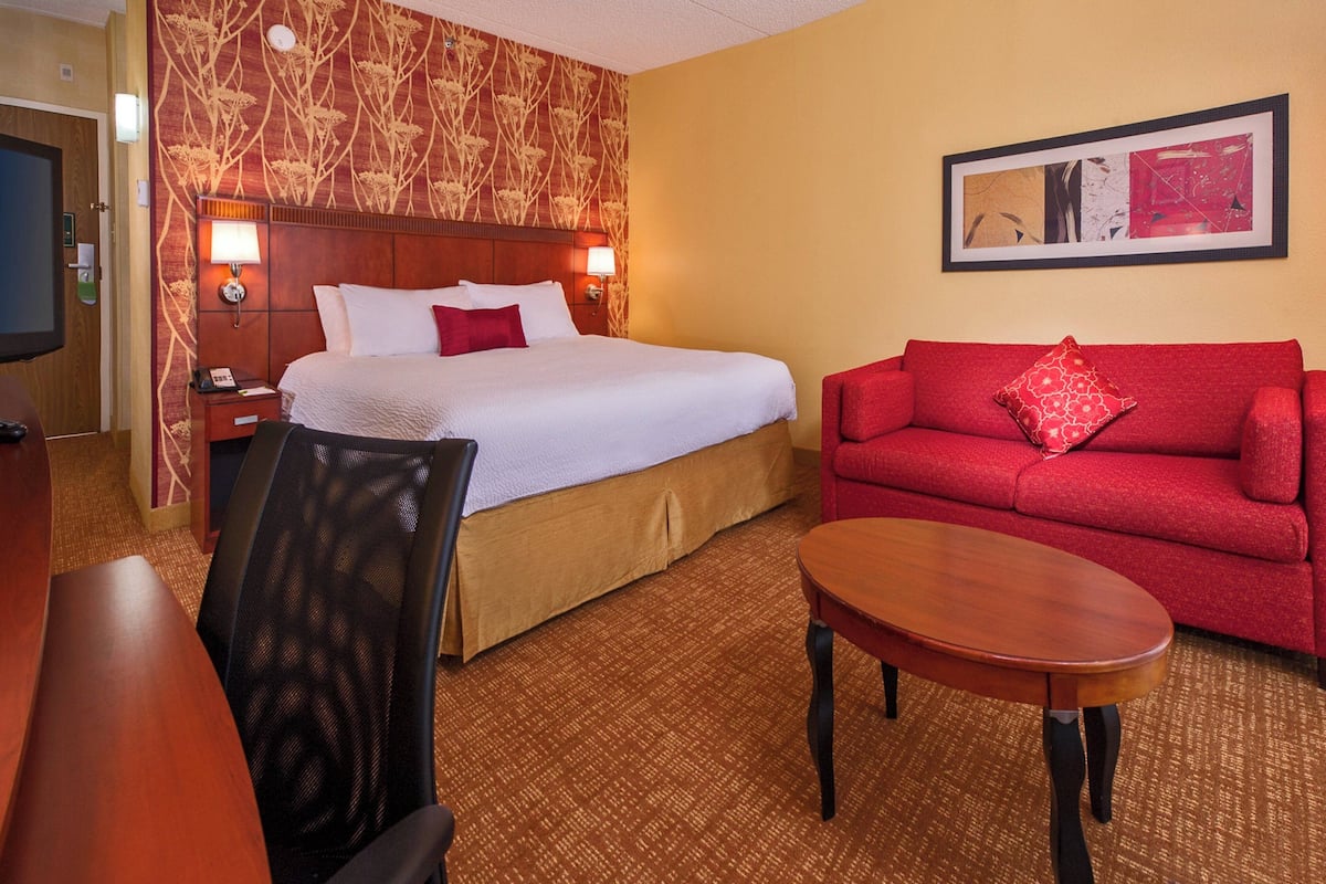 Una habitación de hotel con una cama grande, un sofá rojo, una mesa de madera y un televisor.
