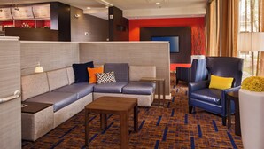 A hotel lobby with a sectional sofa, a wooden coffee table, a blue armchair, and a small table with a lamp.