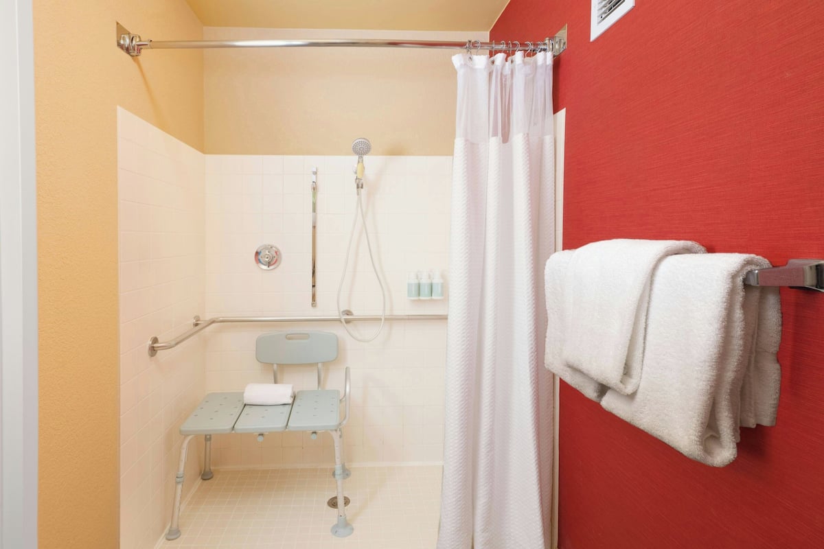Un baño con ducha, barra de apoyo, banco accesible para sillas de ruedas y un perchero para toallas.