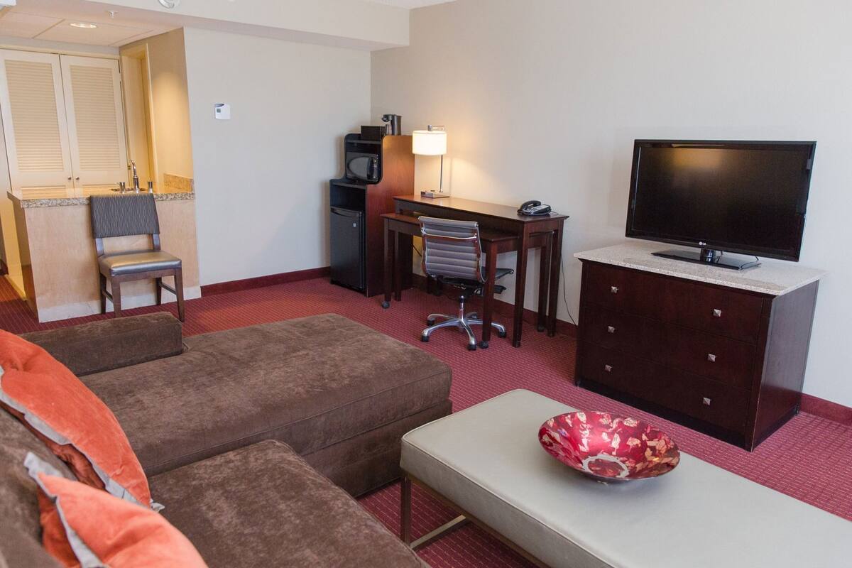 A hotel room with a sofa, a small table, a TV, a desk with a chair, a microwave, and a cabinet.
