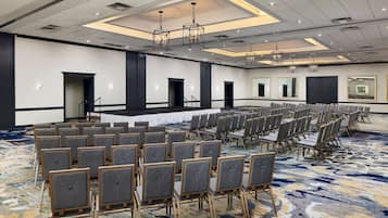 A conference room with rows of chairs, a stage, and a carpeted floor.