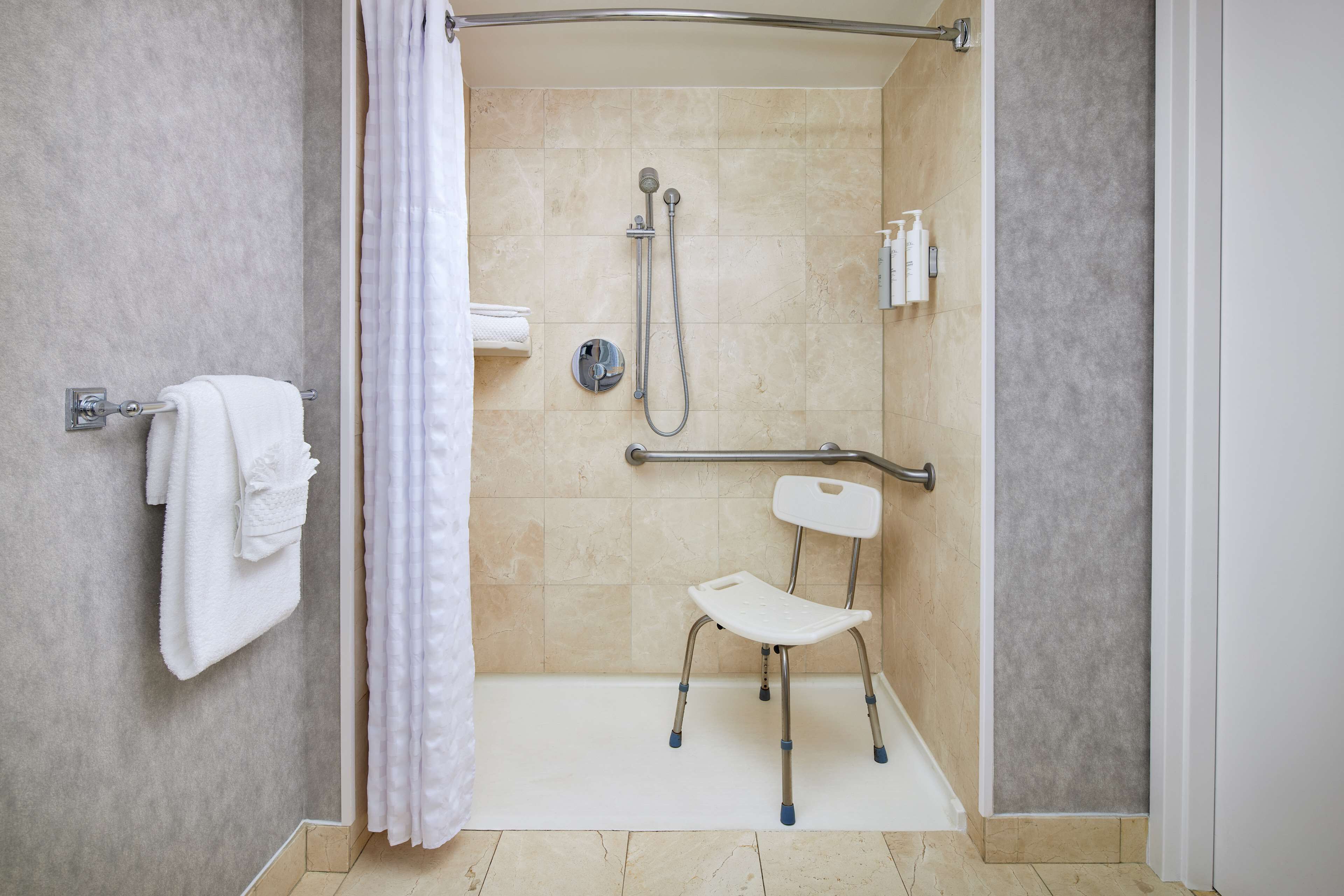 Un espace douche équipé d’un siège de douche, de barres d’appui et d’un porte-serviettes.