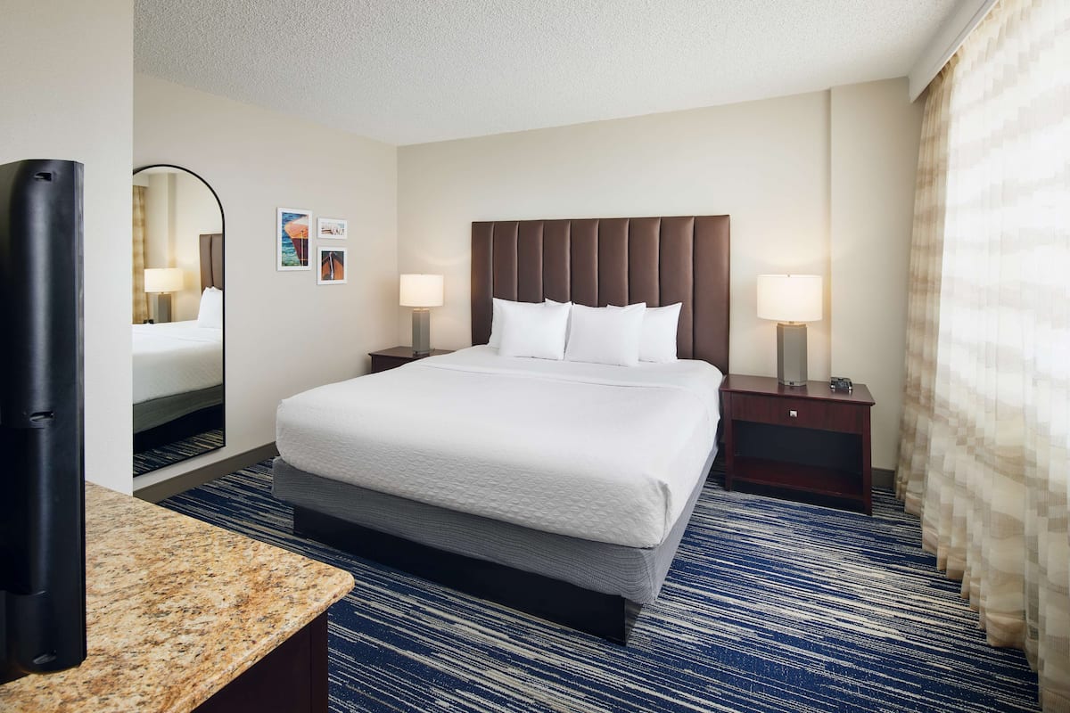 A hotel room with a large bed, two bedside tables with lamps, a mirror, and a carpeted floor.