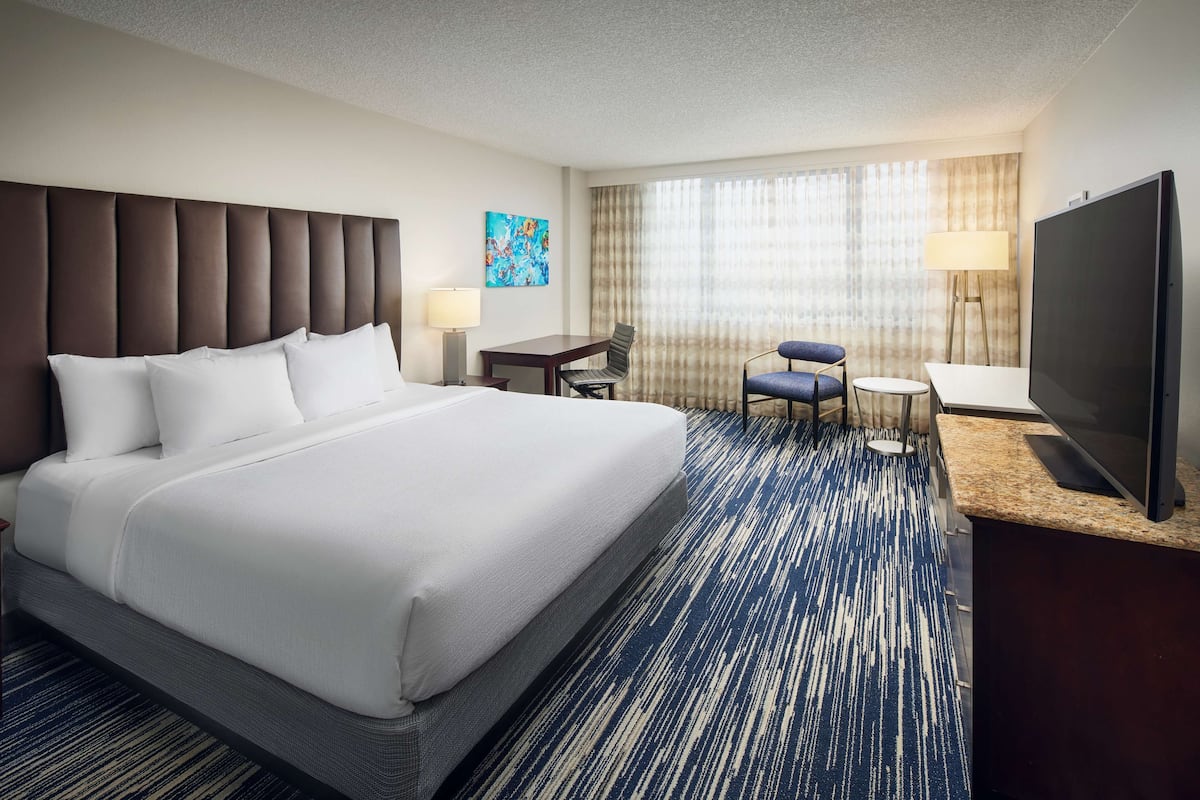 A hotel room with a large bed, a desk with a chair, a television, and a window with curtains.