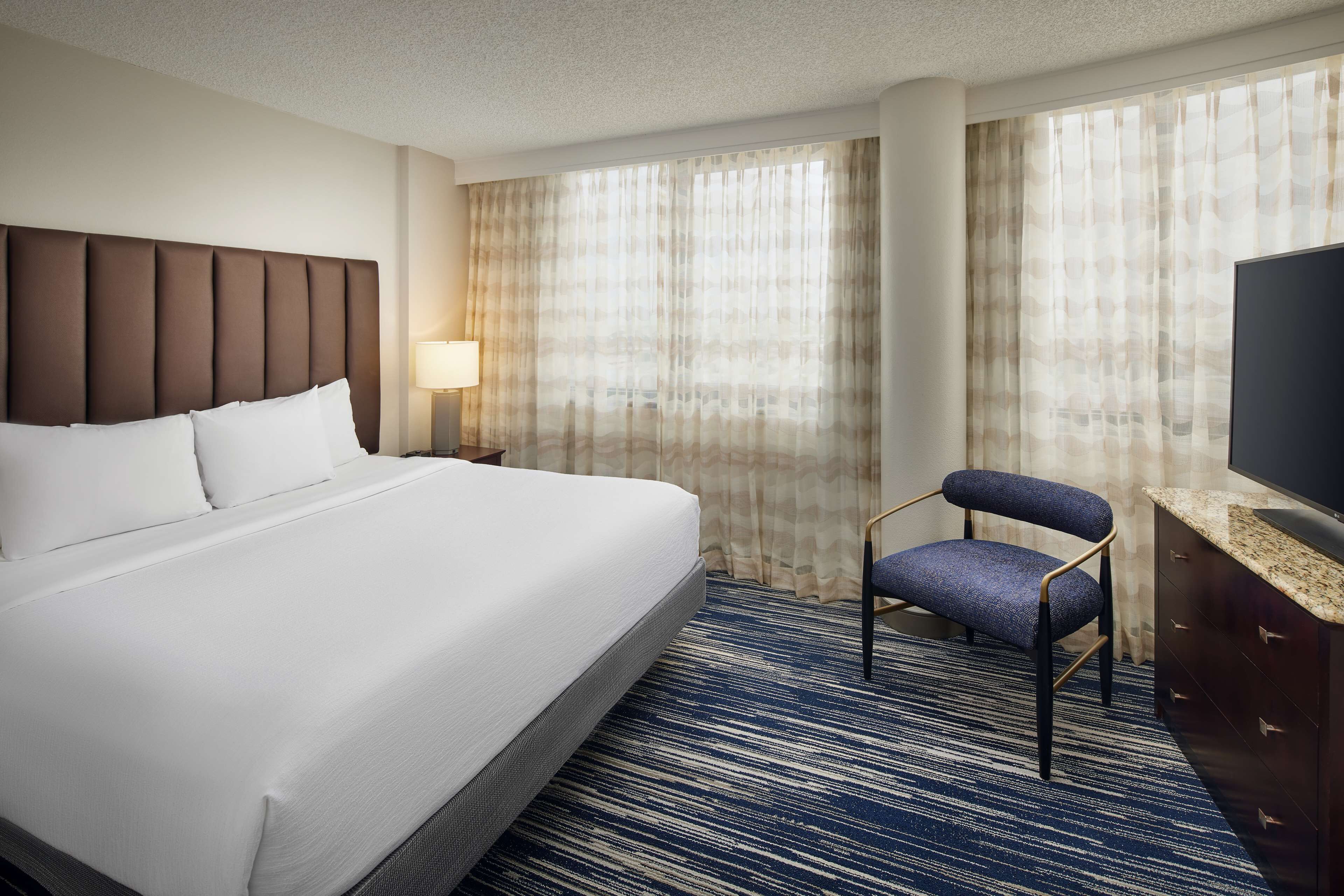 Una habitación de hotel con una cama grande, una silla, un televisor y cortinas.