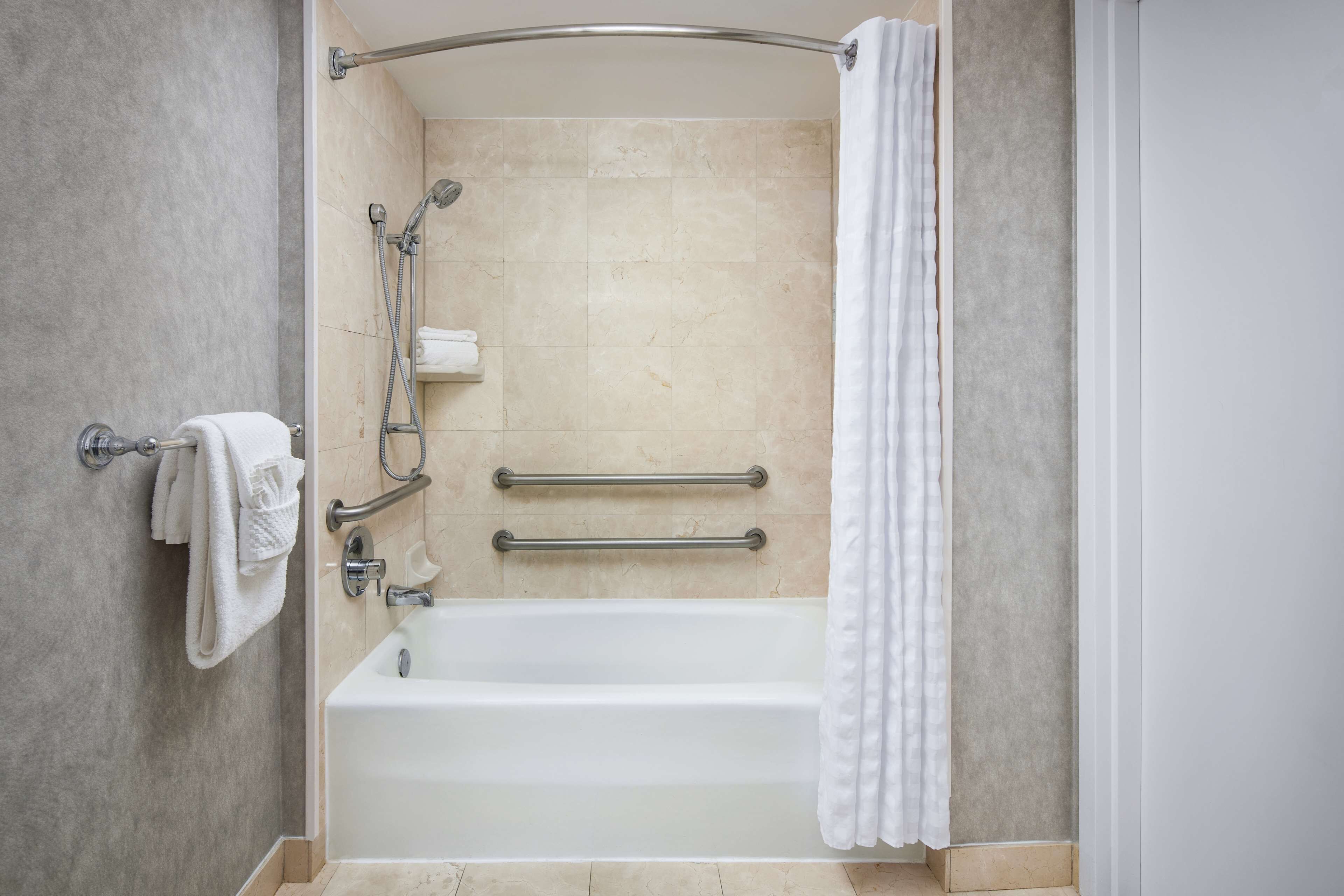 Een moderne badkamer met een bad, handgrepen en een douchegedeelte.