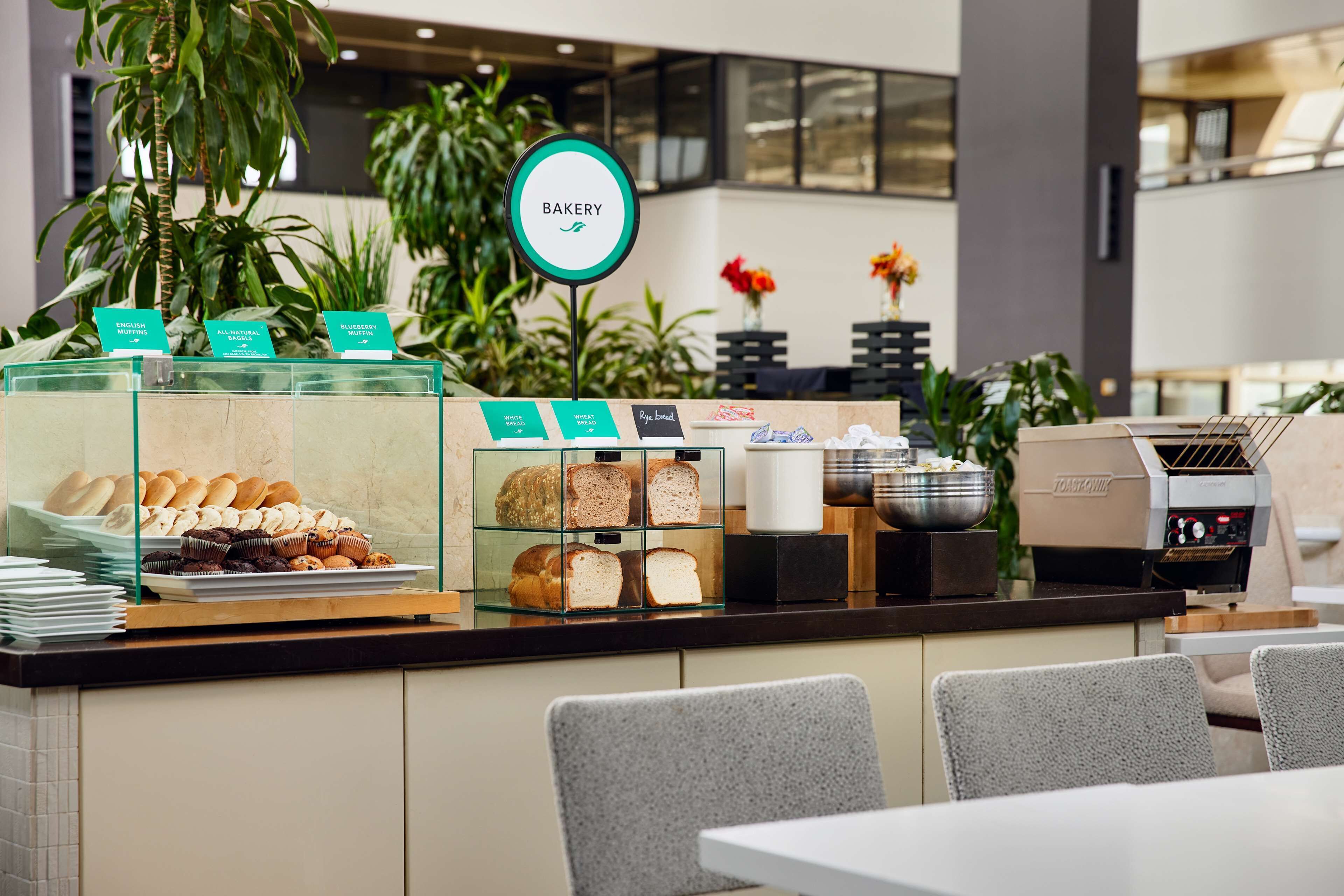 Eine Bäckereitheke mit verschiedenen Backwaren, einer Kaffeemaschine und einem Schild, das Optionen in Englisch, natürlich und glutenfrei anzeigt.