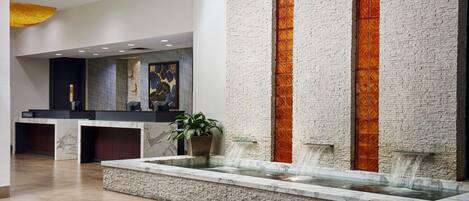 A lobby with a marble reception desk, a water feature, and a textured wall.