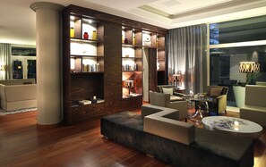 A modern living room with a wooden bookshelf, comfortable seating, and a large window with curtains.