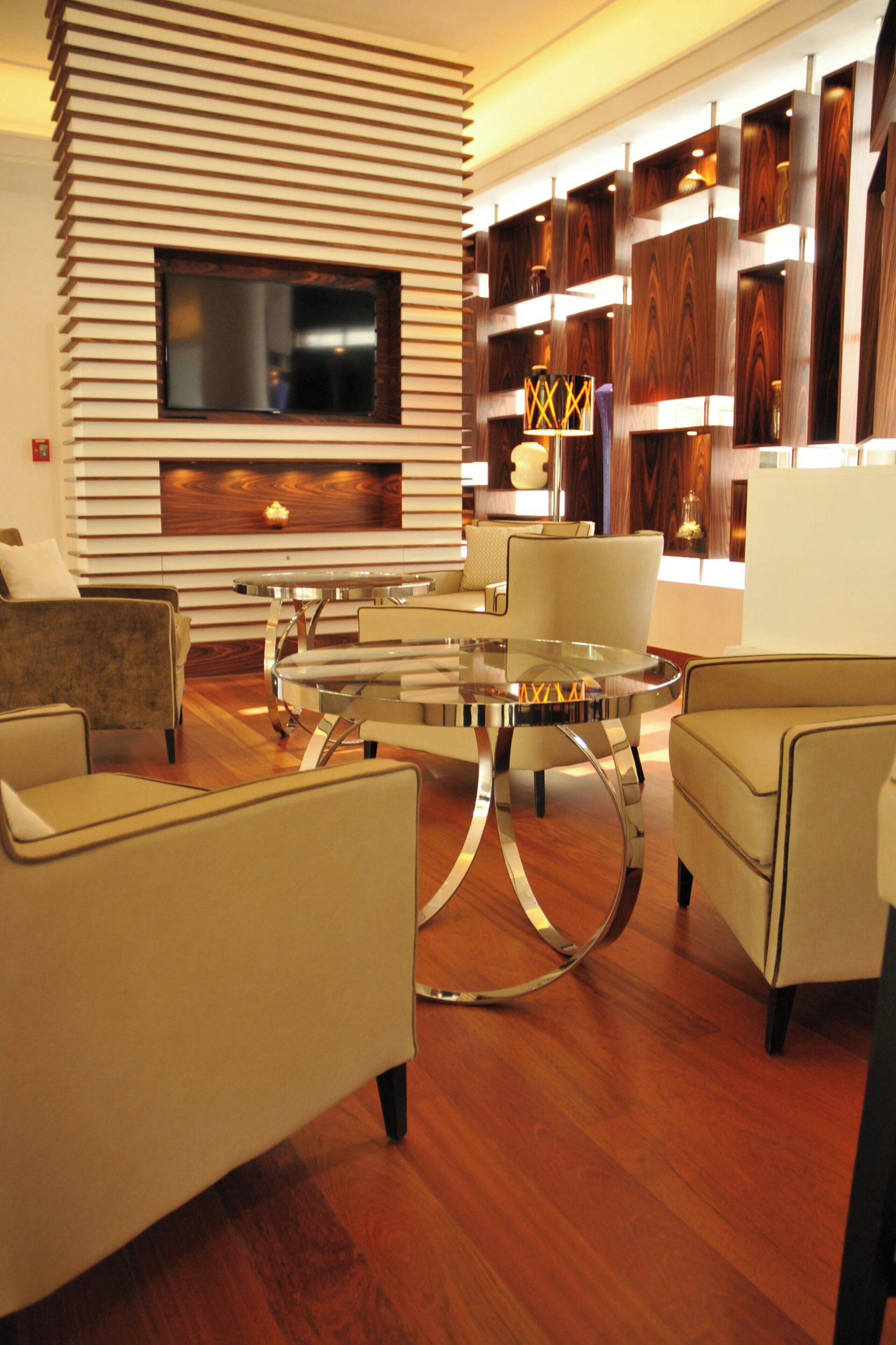 A modern living room with a glass coffee table, beige sofas, and a wooden wall with built-in shelves.