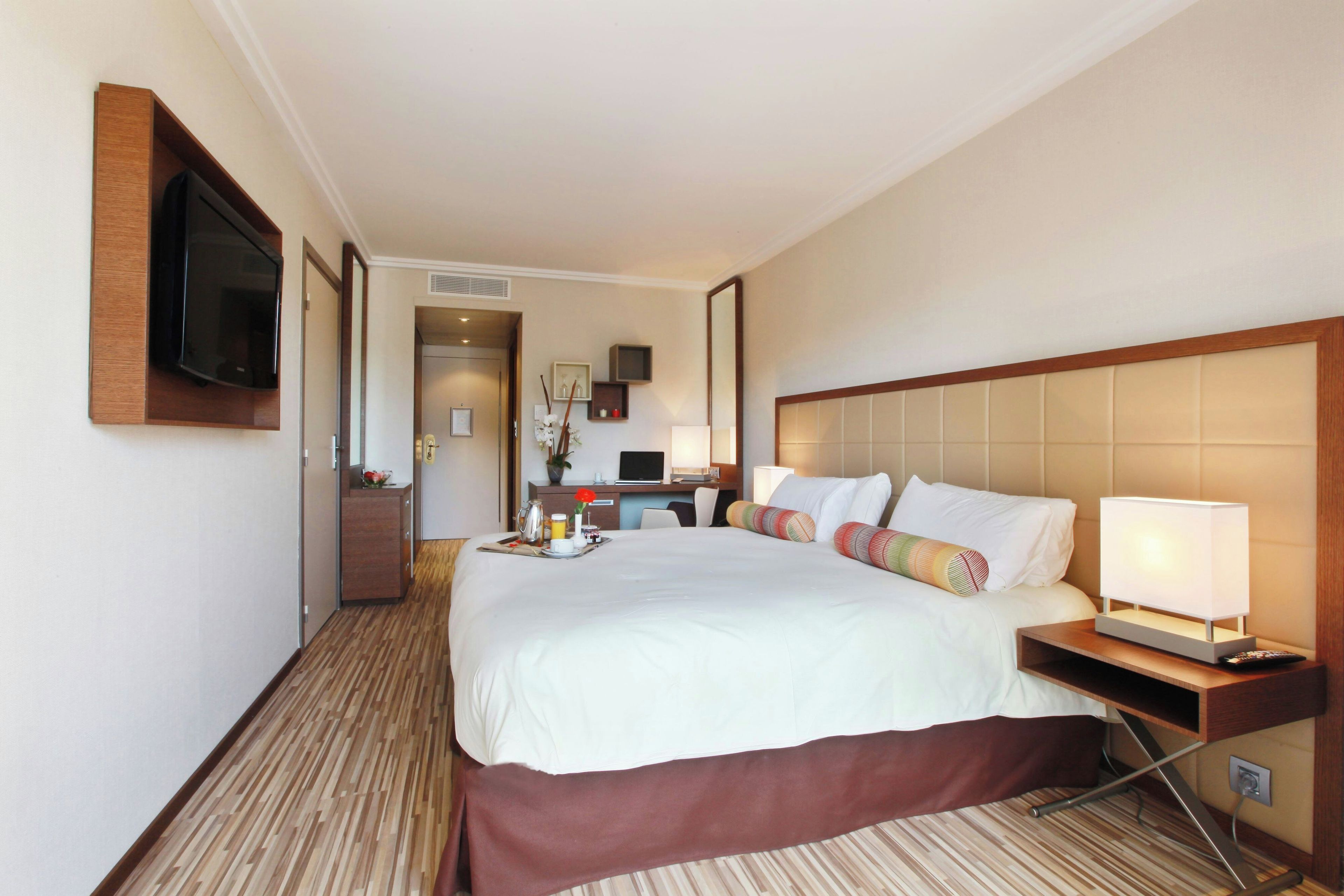 A hotel room with a large bed, bedside table, TV, and a desk with a chair.