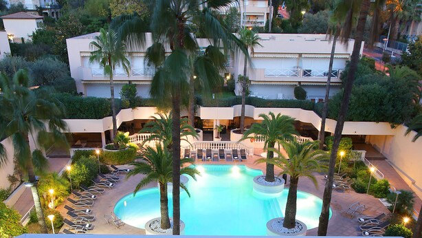 A dining table set with a salad, wine glasses, and a bottle of champagne, overlooking a pool with palm trees and a view of the surrounding buildings.