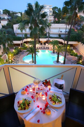 A dining table set with a salad, wine glasses, and a bottle of champagne, overlooking a pool with palm trees and a view of the surrounding buildings. - AC Hotel by Marriott Ambassadeur Antibes - Juan Les Pins (Antibes)
