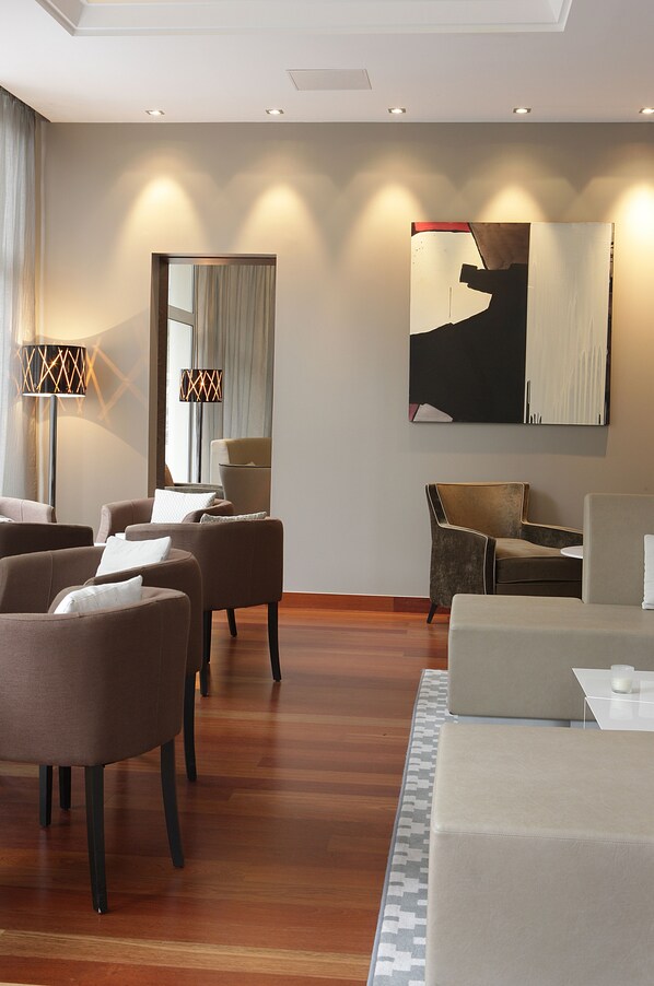 A modern hotel room with a wooden floor, a large abstract painting, and a seating area with sofas and a chair.
