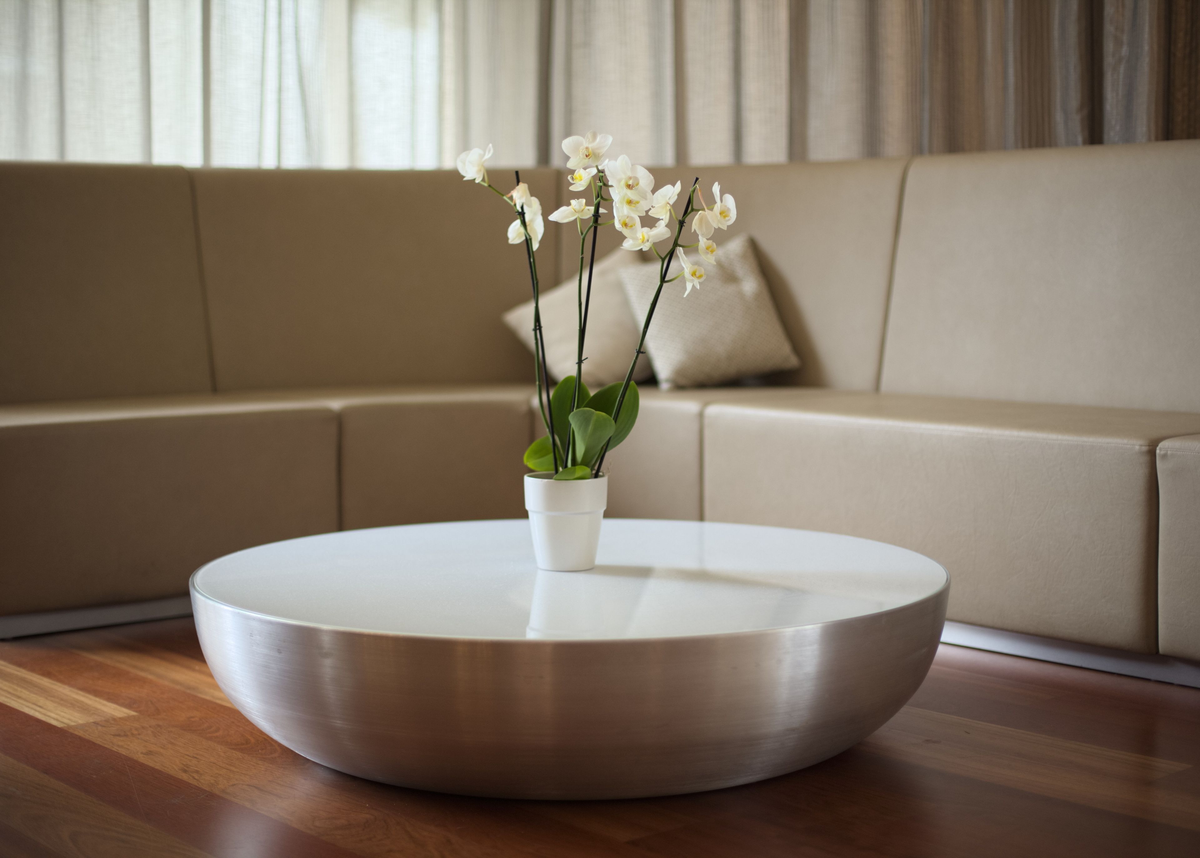 Een ronde, metalen salontafel met een vaas met witte orchideeën op een houten vloer.
