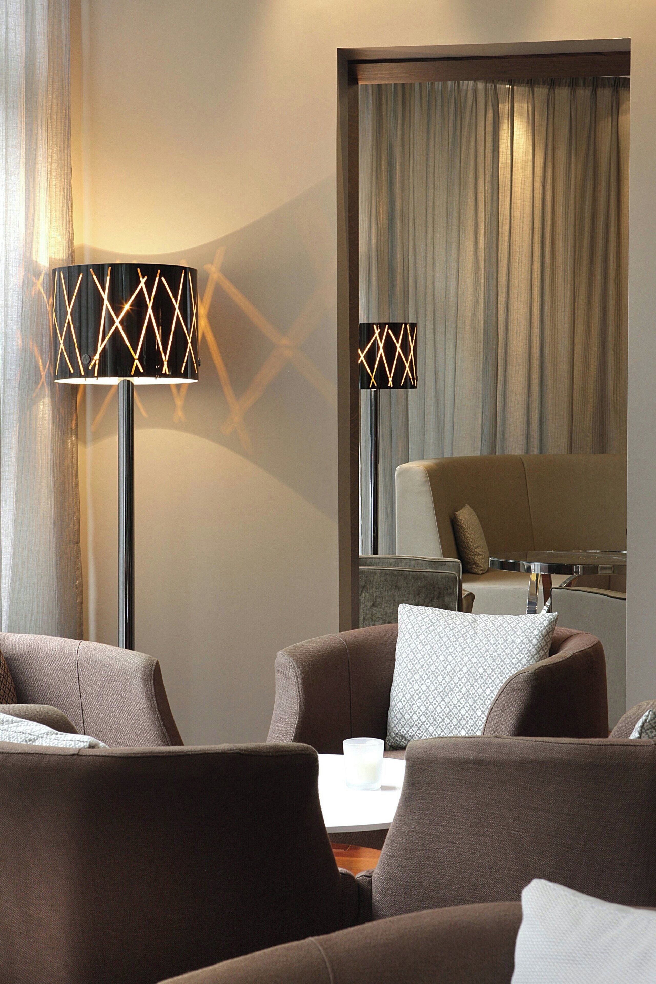 Une chambre d’hôtel moderne, dotée d’un canapé, d’une table avec une bougie et de deux lampadaires aux motifs géométriques.
