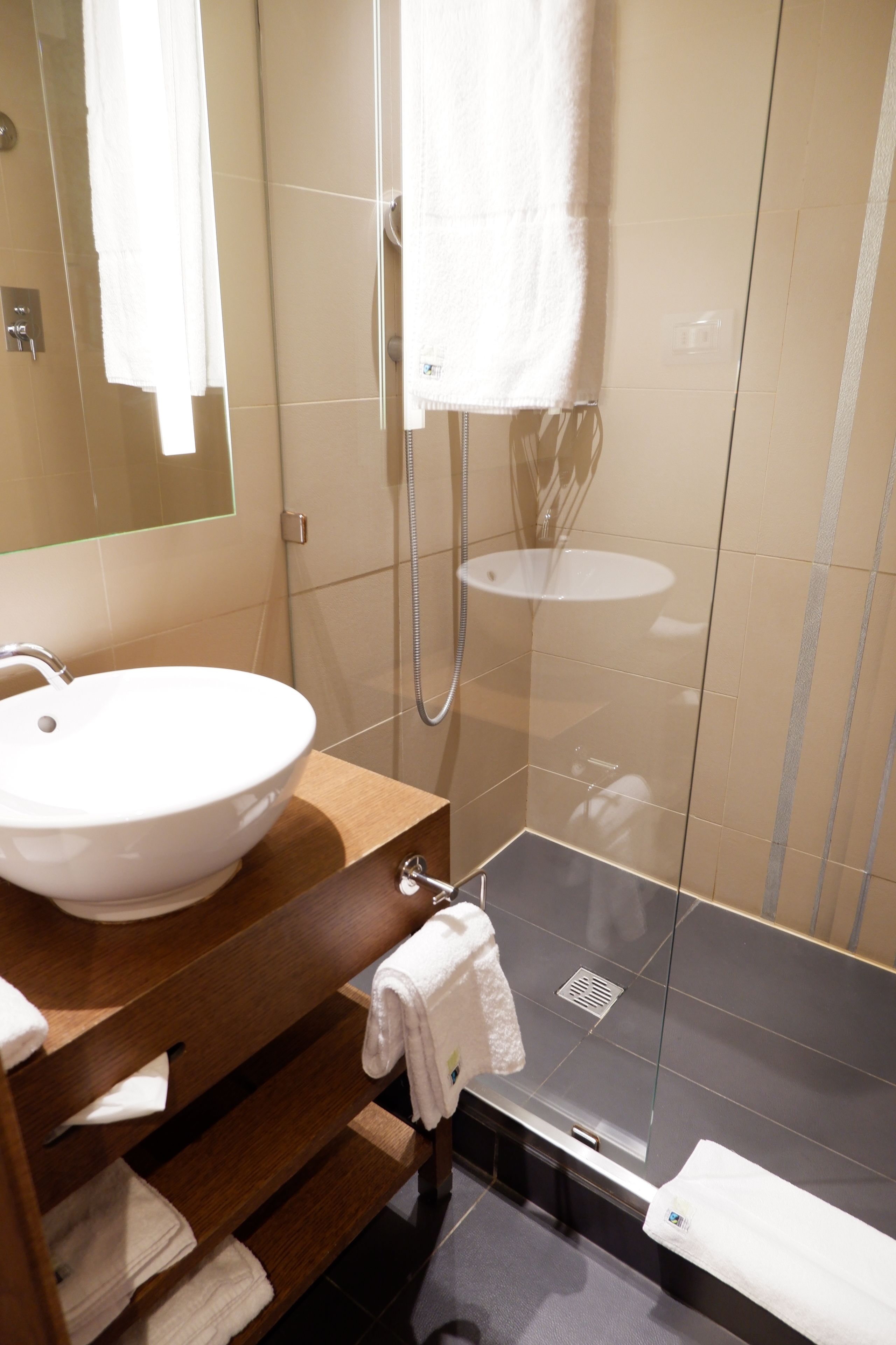 Un baño moderno con lavamanos blanco, tocador de madera, cabina de ducha de vidrio y un perchero para toallas.