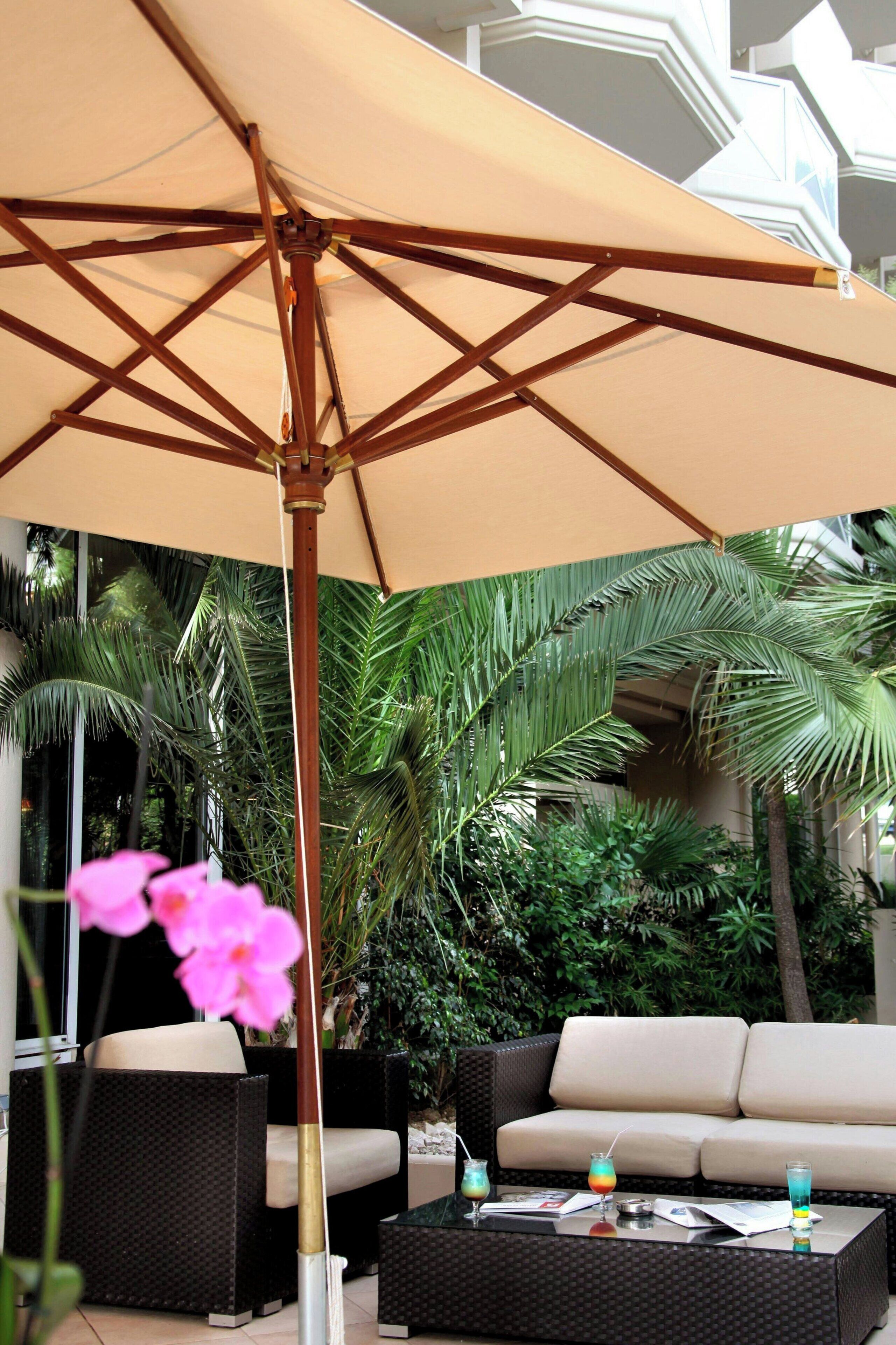An outdoor seating area with a large umbrella, wicker furniture, and lush greenery in the background.