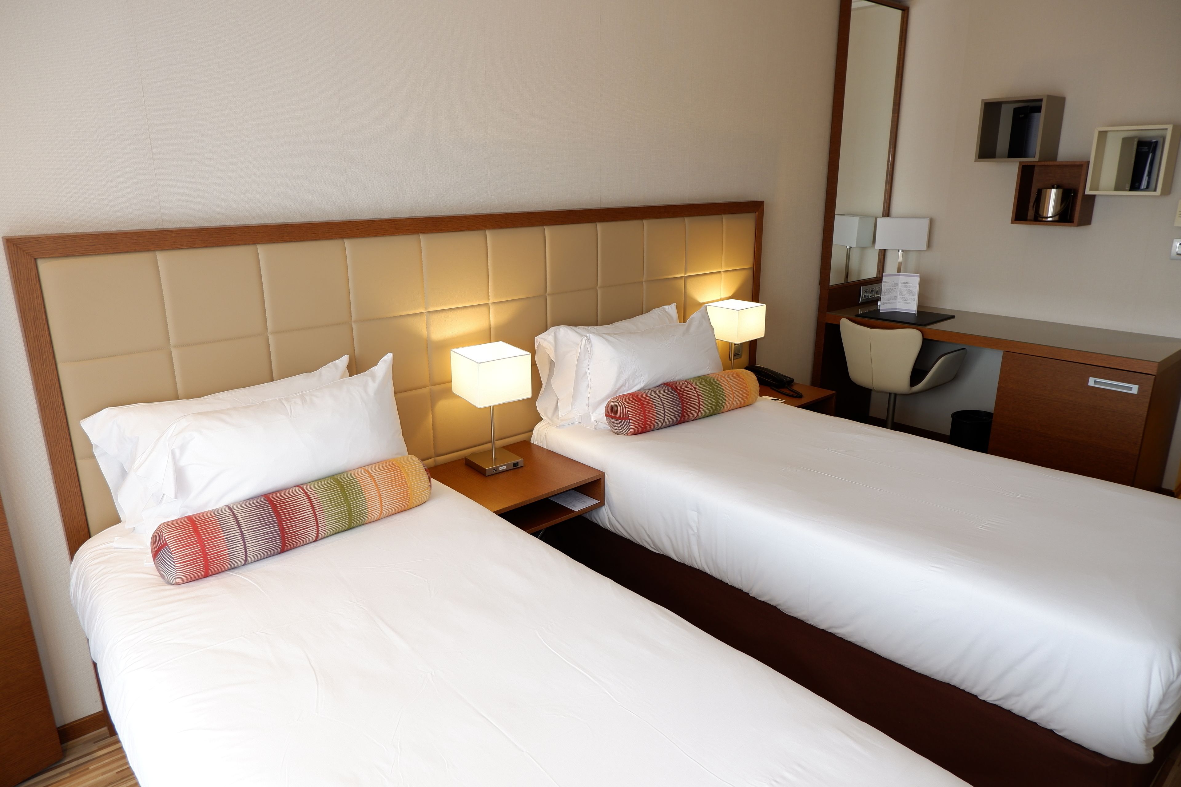 Een hotelkamer met twee enkele bedden, een bureau, een stoel, een spiegel en een klein kastje.