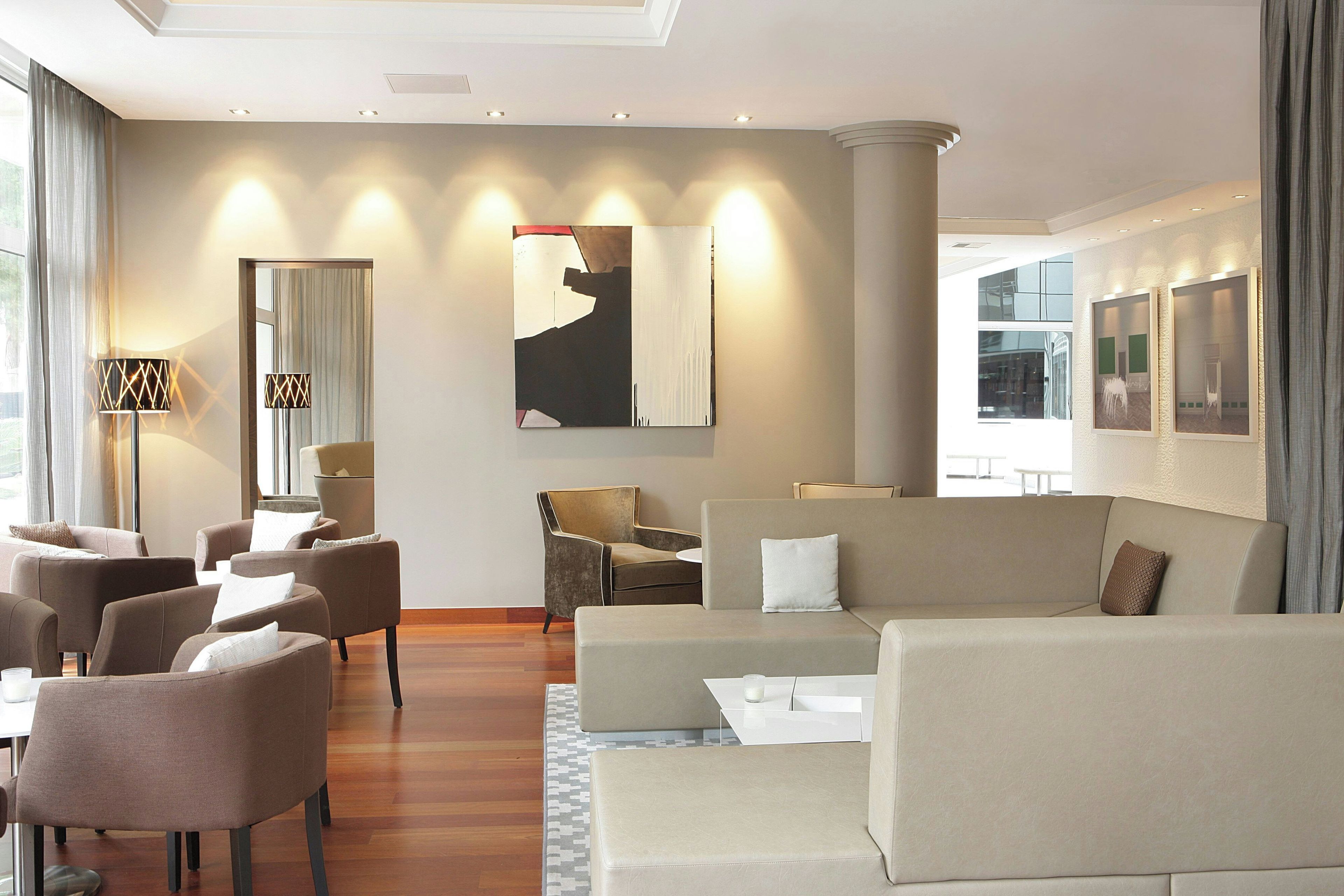 A modern hotel lobby with a seating area, a large abstract painting, and a view of the outside.