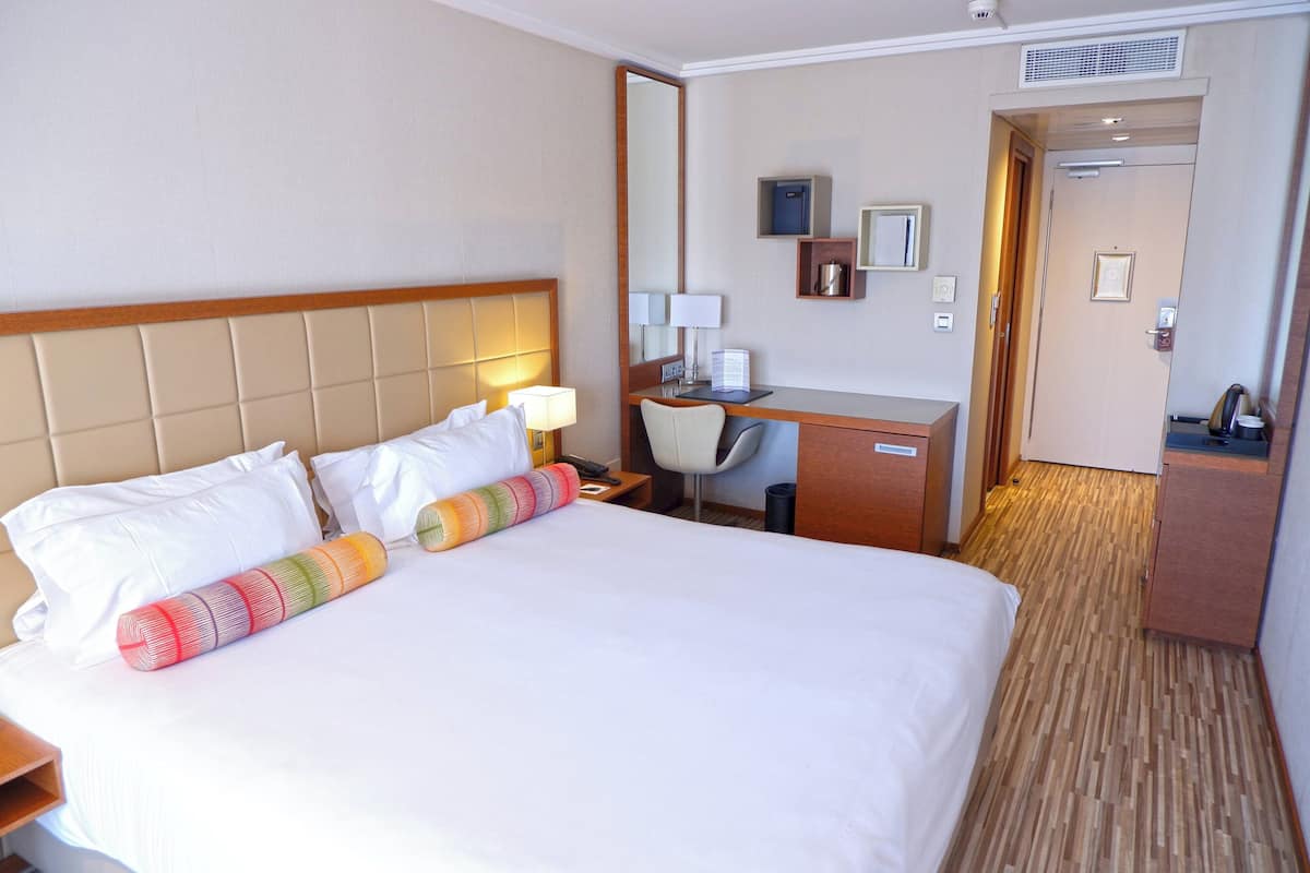 Ein Hotelzimmer mit einem großen Bett, einem Schreibtisch, einem Stuhl und einer kleinen Küchenzeile.