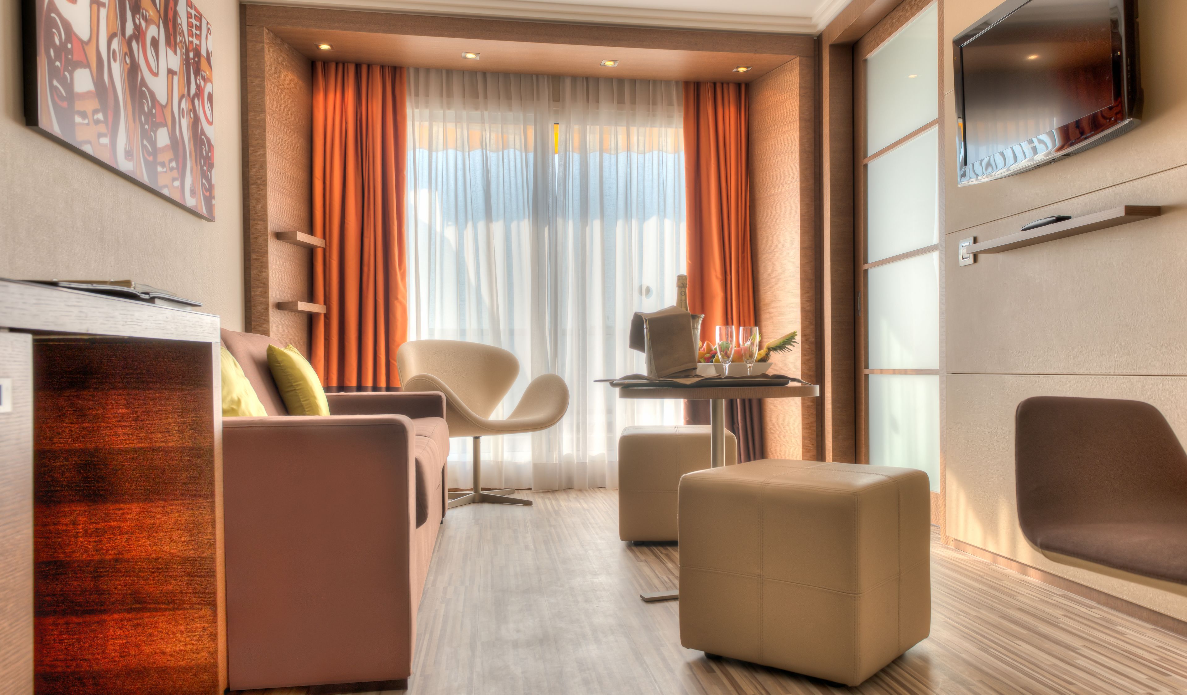 Une chambre d’hôtel moderne équipée d’un canapé, de fauteuils, d’une petite table avec un ordinateur portable et d’un téléviseur fixé au mur.