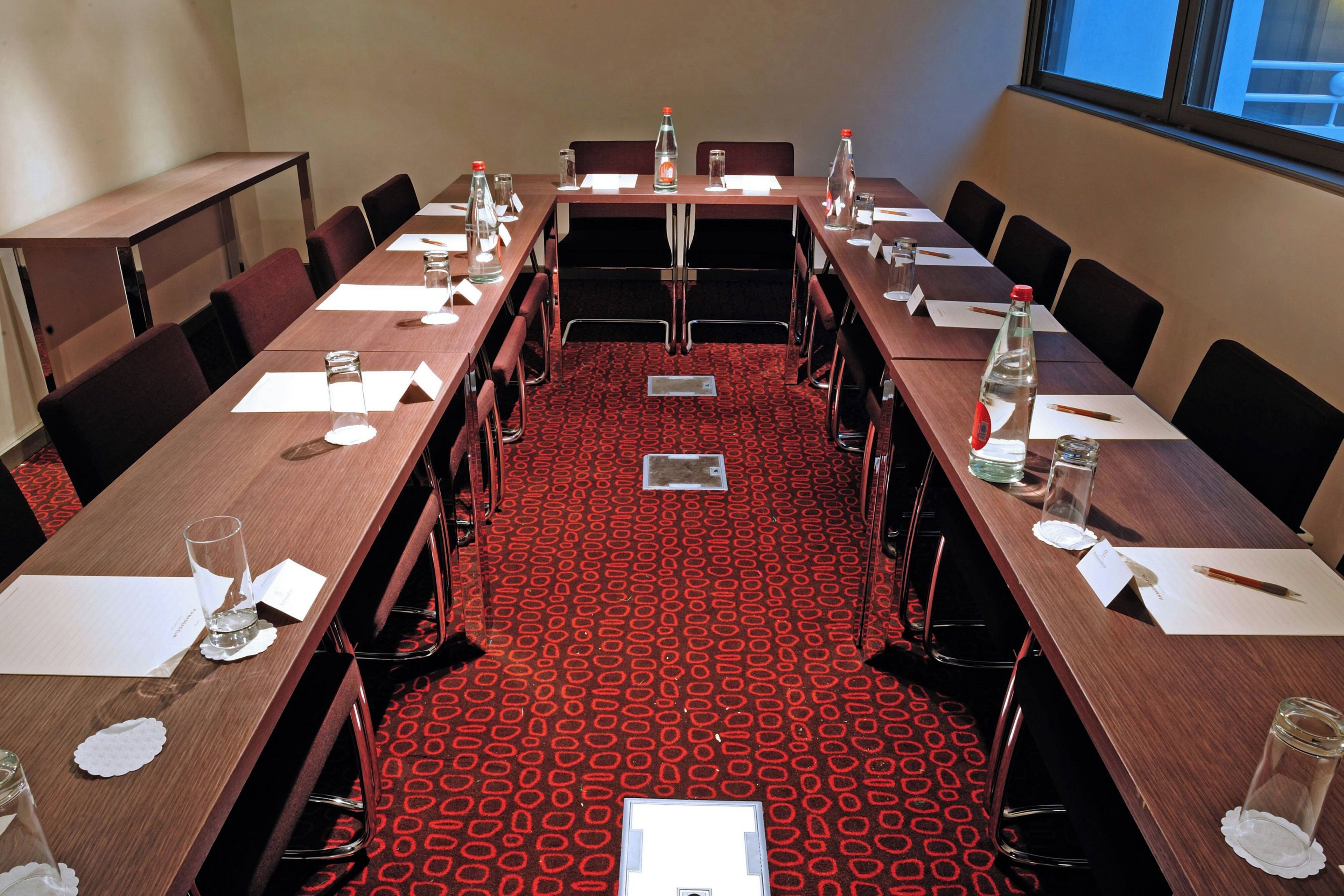 A conference room with long tables, chairs, nameplates, water bottles, and glasses.