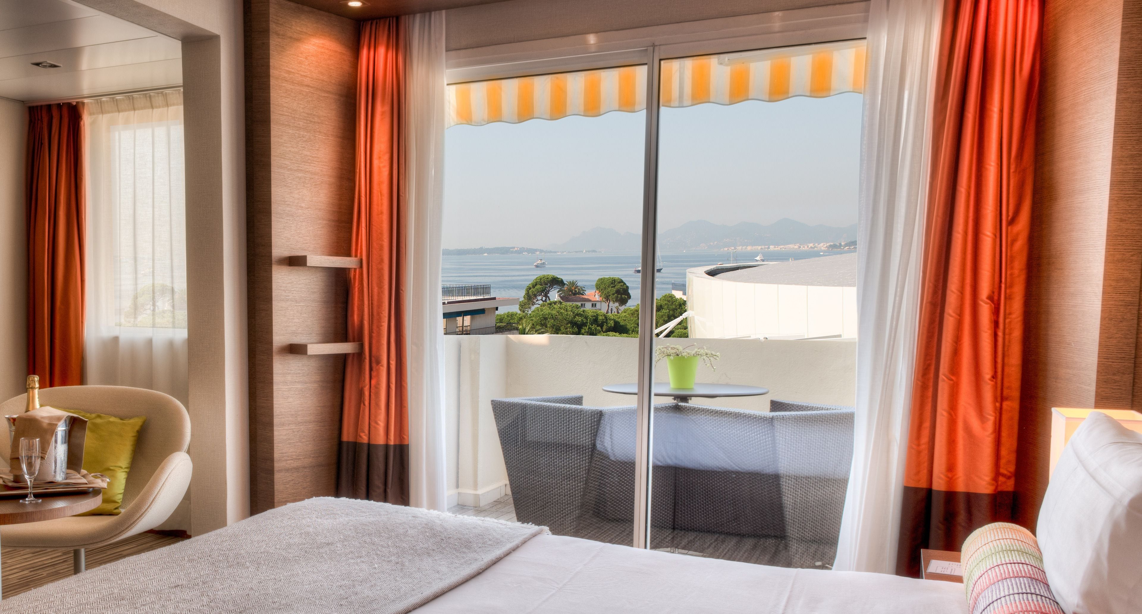 Une chambre d’hôtel comprenant un lit, une chaise, une table et un balcon avec vue sur la mer et les montagnes.