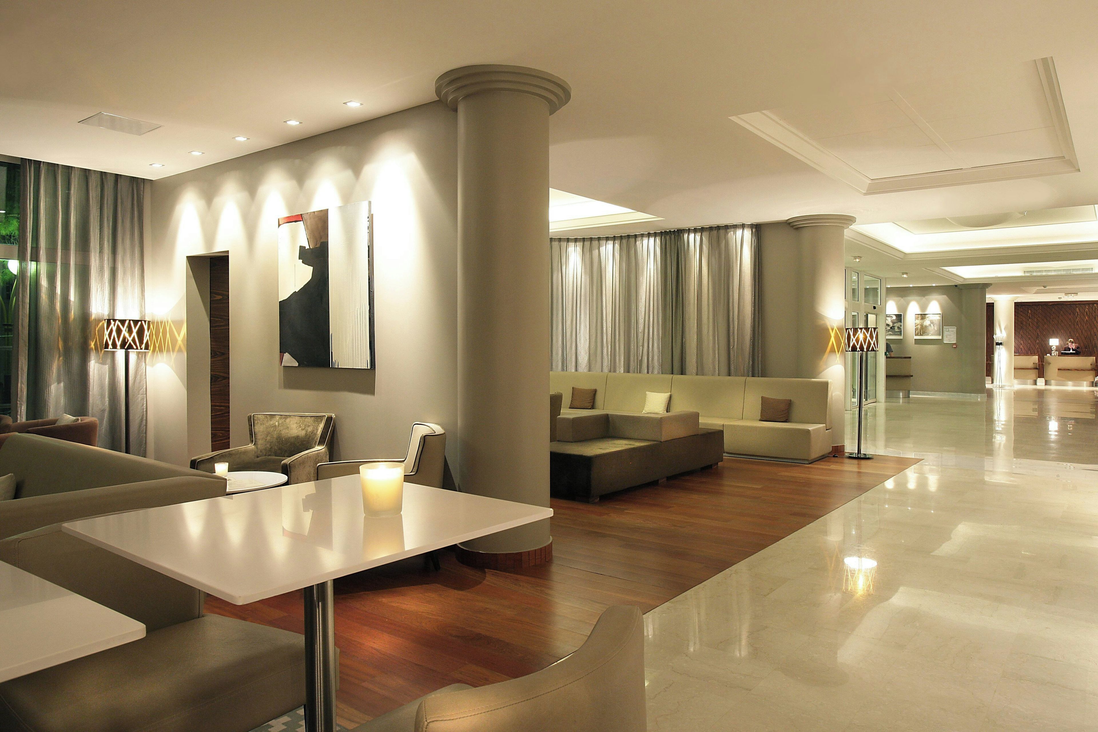 A modern hotel lobby with a seating area, a reception desk, and a large artwork on the wall.