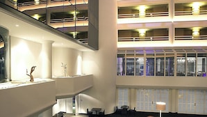 Vestíbulo de hotel de varios niveles con una zona de estar central, una escalera y vistas de la ciudad a través de amplias ventanas.