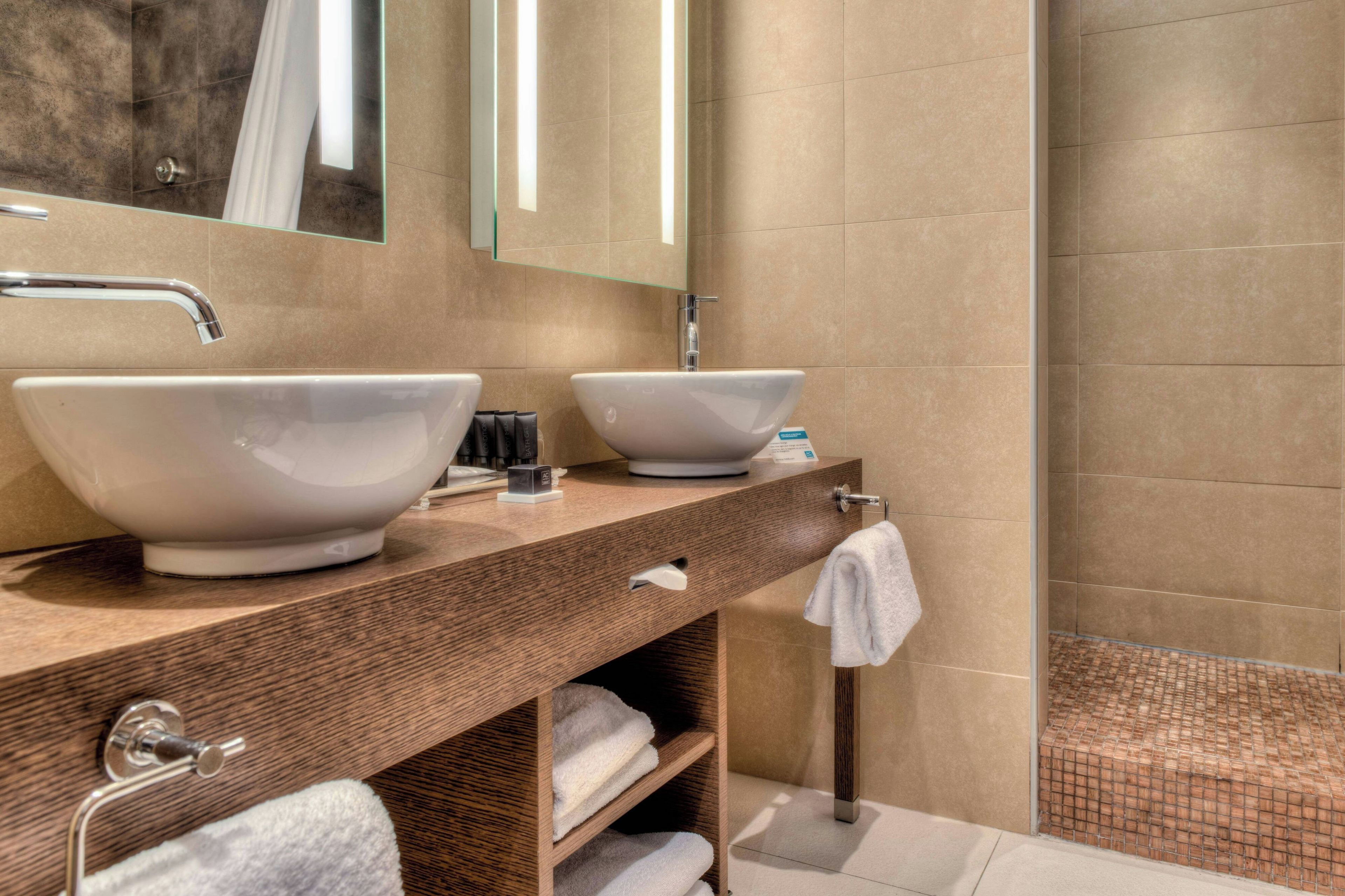 A modern bathroom with two vessel sinks, a wooden vanity, a towel rack, and a glass shower enclosure.
