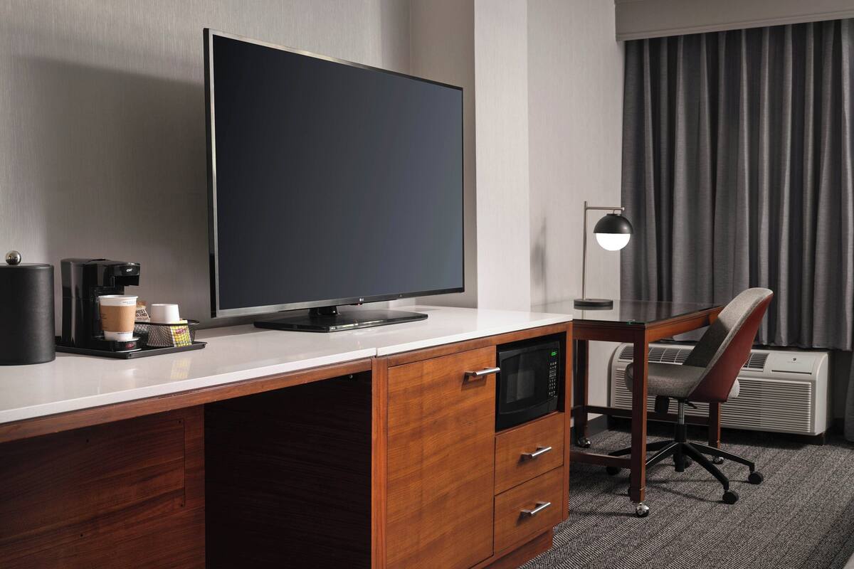 Une chambre d’hôtel équipée d’une télévision à écran plat, d’une machine à café, d’un bureau avec une chaise et d’un appareil de climatisation.