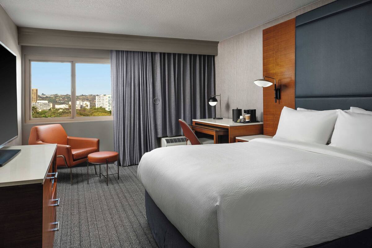 Une chambre d’hôtel avec un grand lit, un bureau, une chaise et une vue sur la ville par la fenêtre.