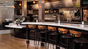 Zona de bar moderna con una barra curva, taburetes y un panel con bebidas y aperitivos.