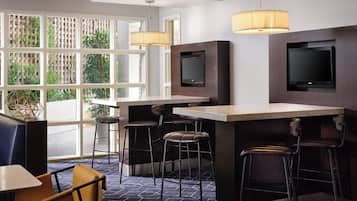 A modern bar area with two TVs, bar stools, and pendant lights.